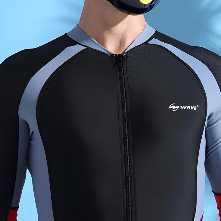 Homme portant une combinaison de plongée intégrale noire, grise et rouge, la main sur le front pour se protéger du soleil.