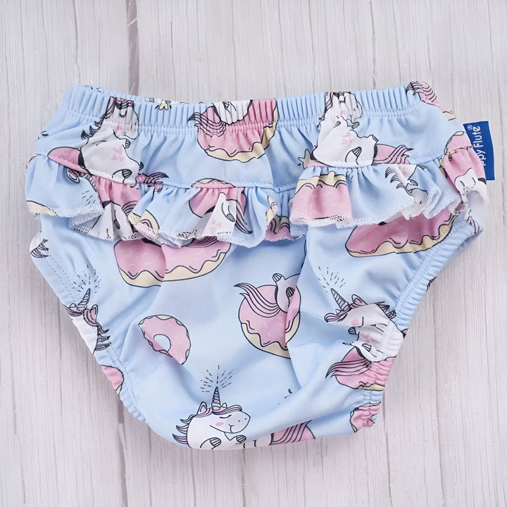 Culotte d'apprentissage pour bébé avec motif licorne et beigne sur fond bleu, détails à volants.