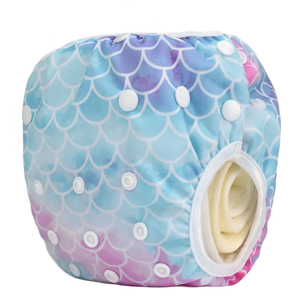 Couche de bain réutilisable avec un motif d'écailles de sirène bleues, violettes et roses. Fermetures à boutons-pression blanches sur les côtés. Bords garnis de blanc.