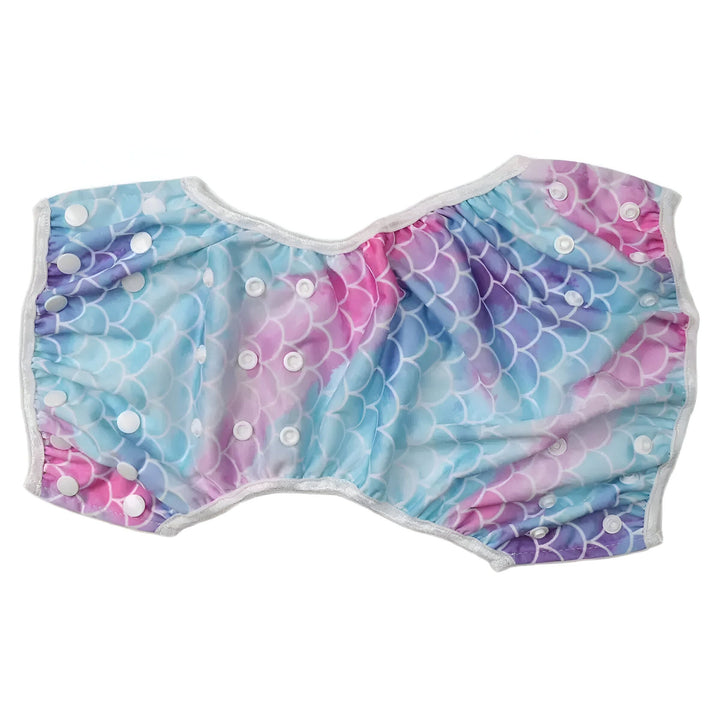 Couche lavable réutilisable pour bébé avec motif écailles de sirène bleues et roses, fermetures à boutons-pression blancs et doublure absorbante blanche visible.