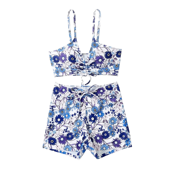 Femme souriante portant un ensemble de bain deux pièces avec un motif floral coloré sur fond noir, comprenant un haut noué et un short. Vêtements de plage tendance.