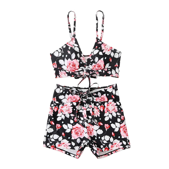 Femme souriante portant un ensemble de bain deux pièces à fleurs bleues et blanches, comprenant un haut court à bretelles et un short taille haute avec cordon de serrage. Idéal pour la plage ou la piscine.