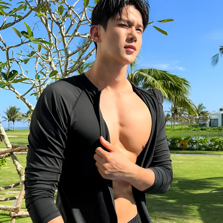 Homme asiatique souriant près d'une piscine, portant un ensemble de protection solaire noire : chemise à manches longues, legging et short. Vêtements de plage anti-UV pour la natation et les activités aquatiques.