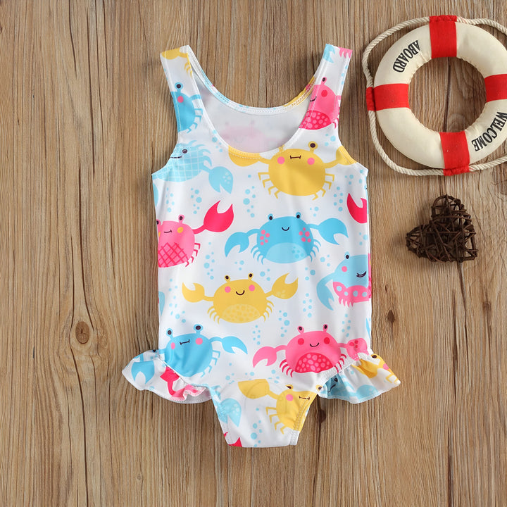 Gros plan sur un maillot de bain pour bébé, blanc avec des motifs de crabes bleus, roses et jaunes. Idéal pour les vacances à la plage ou à la piscine.