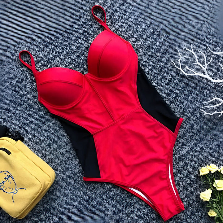 Femme en maillot de bain rouge avec empiècements en mesh noir, posant avec une main dans les cheveux. Style élégant et moderne, parfait pour la plage ou la piscine.