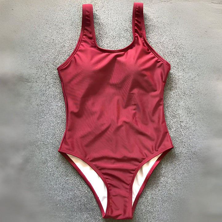 Femme en maillot de bain une pièce blanc sur la plage, dos ouvert. Mer turquoise en arrière-plan.