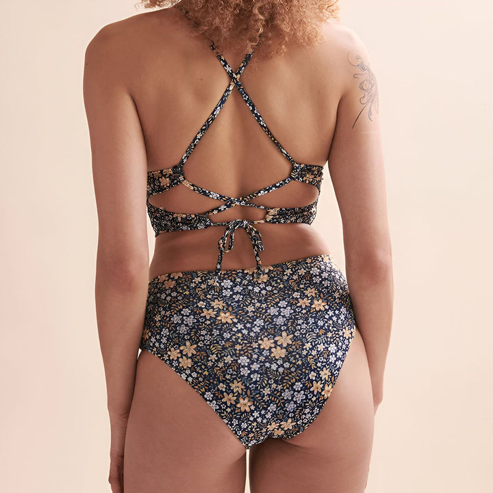 Vue rapprochée d'un maillot de bain une pièce bleu marine à motif floral, dos nu avec des découpes et des lacets croisés. Style estival et tendance.