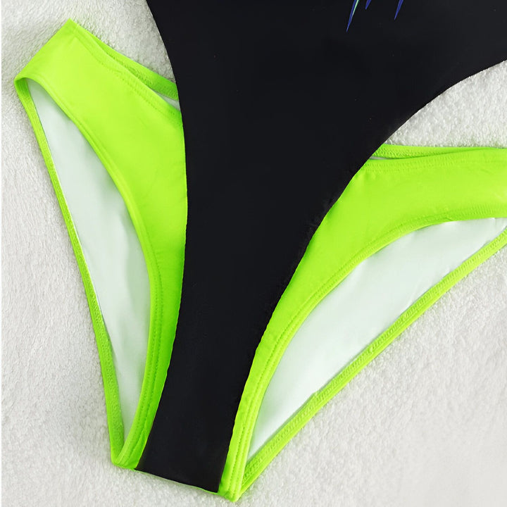 Gros plan d'une femme portant un maillot de bain une pièce noir avec des bordures vert fluo et un motif papillon coloré.