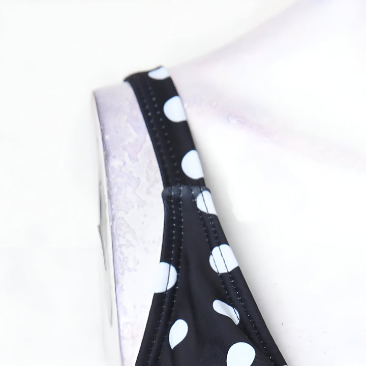 Gros plan d'un maillot de bain noir à pois blancs. Bretelle noire cousue.