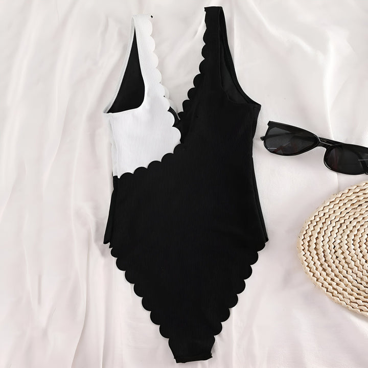 Maillot de bain une pièce bicolore noir et blanc avec bordures festonnées, lunettes de soleil noires et napperon en paille sur fond de tissu blanc.