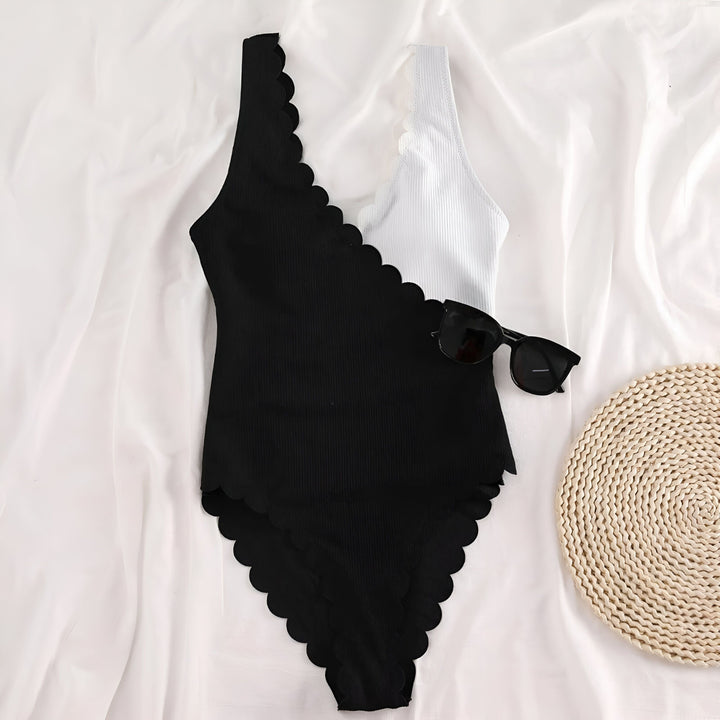 Maillot de bain une pièce noir et blanc à festons, avec des lunettes de soleil noires et un petit tapis en paille ronde sur un drap blanc.