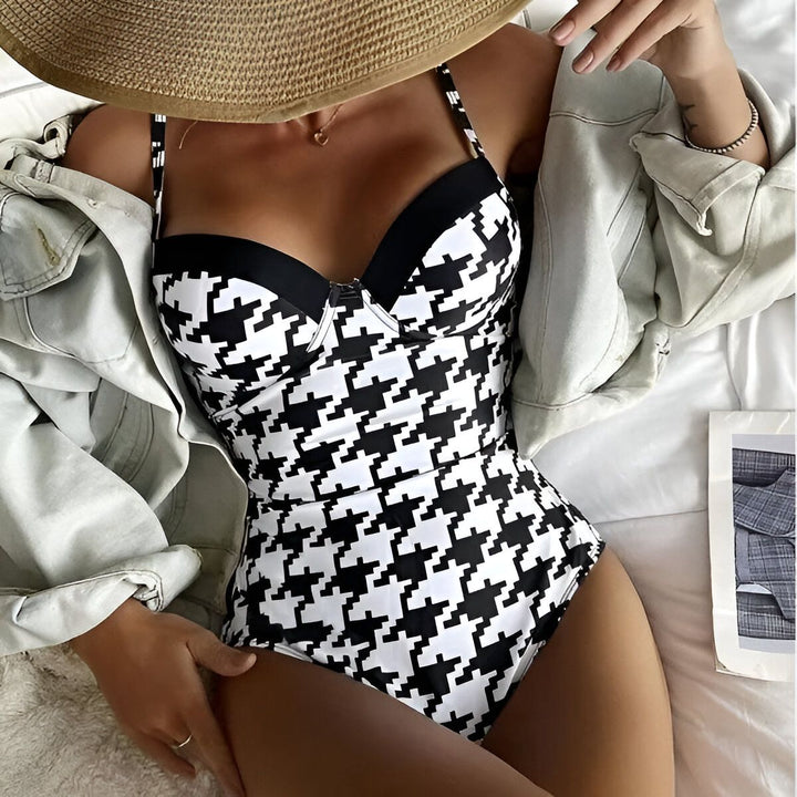 Femme allongée en maillot de bain une pièce pied-de-poule noir et blanc, veste en jean ouverte. Allure décontractée et élégante, mise en avant du motif tendance. Style estival et mode.