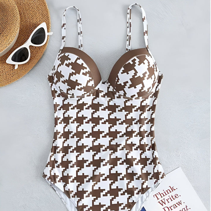 Image d'un maillot de bain une pièce à motif pied-de-poule marron et blanc, posé sur un livre bleu et une carte blanche avec l'inscription "Think, Write, Draw, Repeat". Un flacon de parfum repose sur la carte.