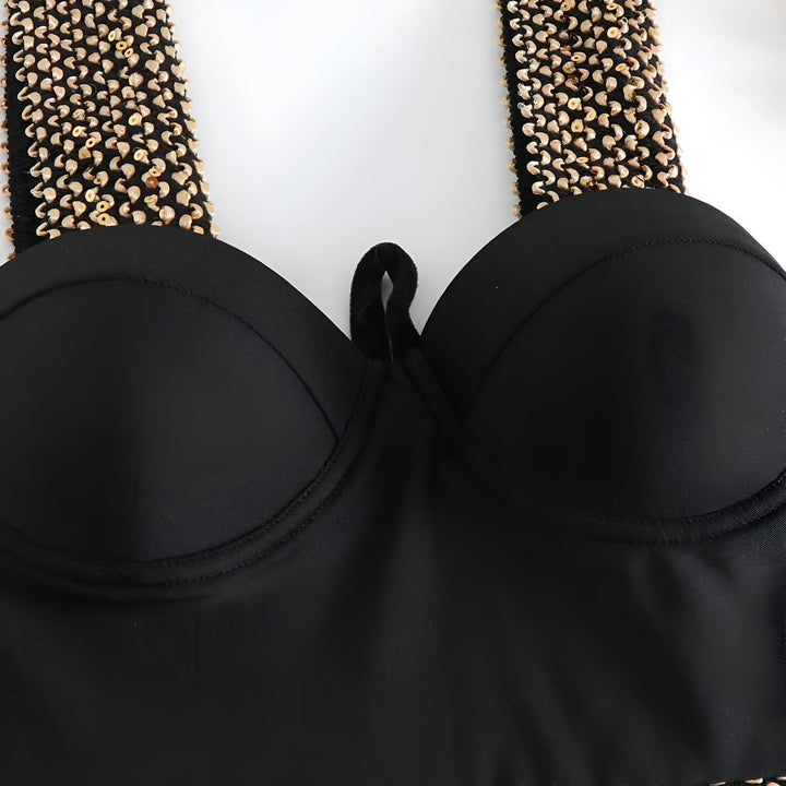 Image rapprochée d'un maillot de bain une pièce noir avec une feuille verte dans le coin inférieur gauche, créant un contraste visuel.