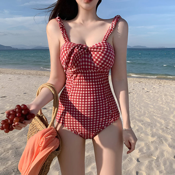 Femme en maillot de bain une pièce rouge et blanc à carreaux sur la plage. Elle tient un sac de plage et du raisin. Mer et ciel bleu en arrière-plan. Mode été.