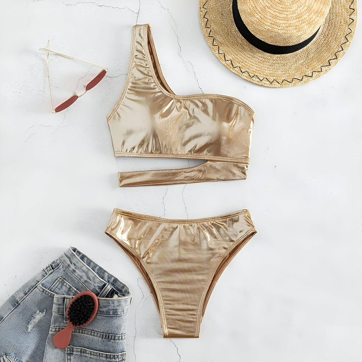 Vue rapprochée d'un bikini une pièce doré brillant sur fond blanc. Haut asymétrique avec découpe. Culotte de bikini taille haute. Idéal pour la plage, la piscine ou une fête estivale.