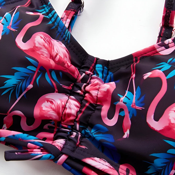 Haut de bikini noir avec motifs de flamants roses et feuilles bleues, détail froncé au centre. Idéal pour la plage et la piscine.