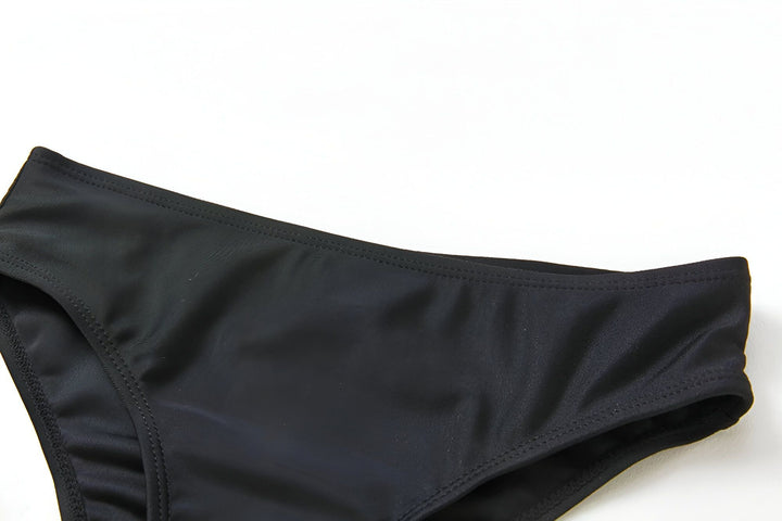 Maillot de bain deux pièces pour fille avec imprimé flamants roses et feuilles tropicales. Culotte de bain noire unie. Décor coquillages et feuille de palmier.