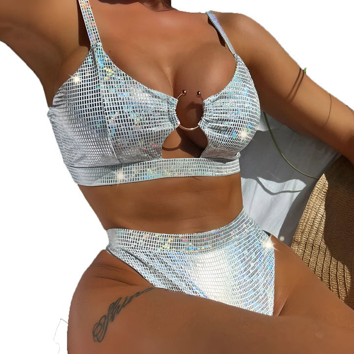 Maillot de bain deux pièces argenté brillant sur un cintre, accompagné d'un sac en toile "Attitude" et de sandales beiges ornées de perles, le tout sur un fond clair et aéré. Accessoires estivaux pour un look chic à la plage.
