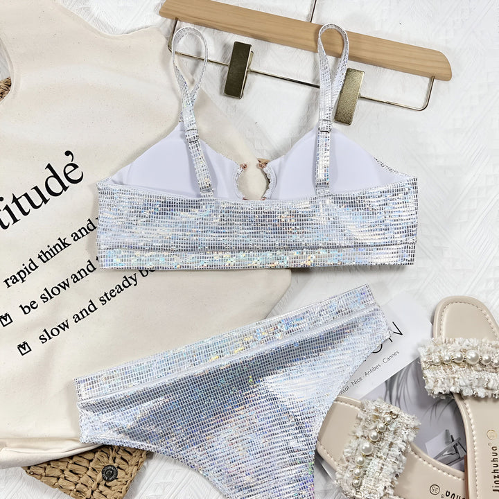 Haut de maillot de bain argenté brillant avec anneau doré, sur un sac en toile écru avec une phrase inspirante imprimée en noir. Détail de la texture et des reflets du tissu.