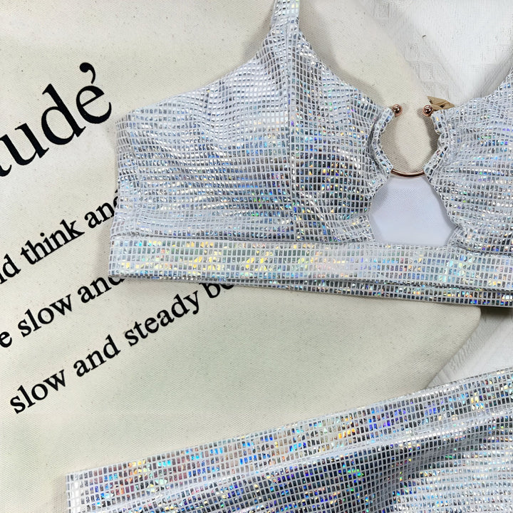 Ensemble de bikini deux pièces argenté scintillant sur un cintre en bois, accompagné d'un sac en toile et de sandales beiges ornées de perles. Vêtements de plage tendance.