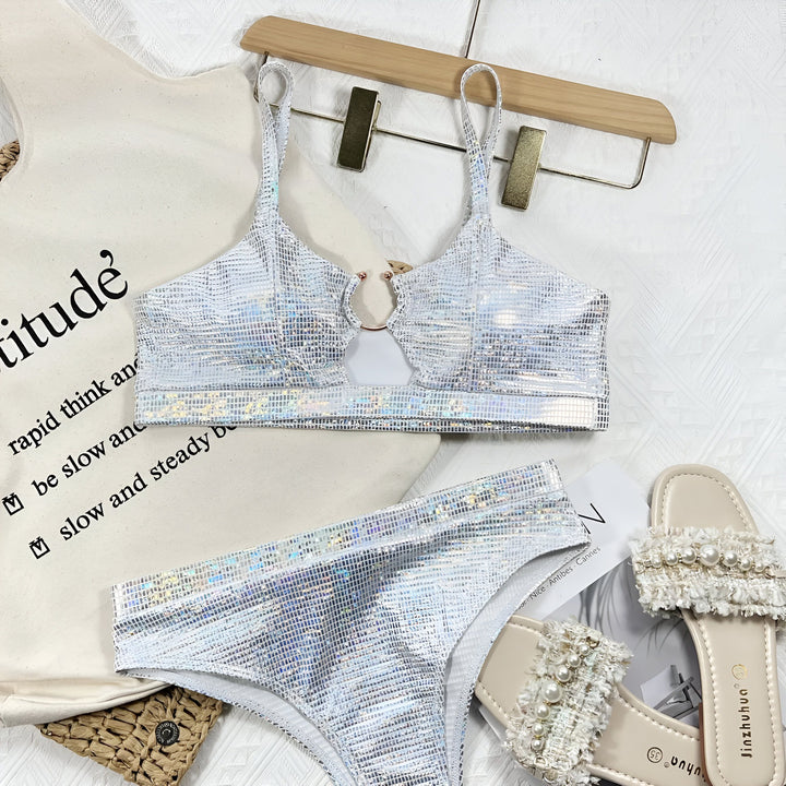 Image d'une femme portant un bikini argenté scintillant avec un anneau décoratif. Elle est assise et bronzée, avec un tatouage visible. Ambiance plage et été.