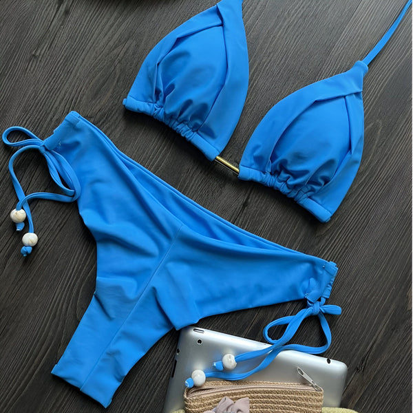 Maillot de bain deux pièces bleu turquoise sur fond bois foncé, avec un iPad et un petit sac. Idéal pour la plage et les vacances d'été.