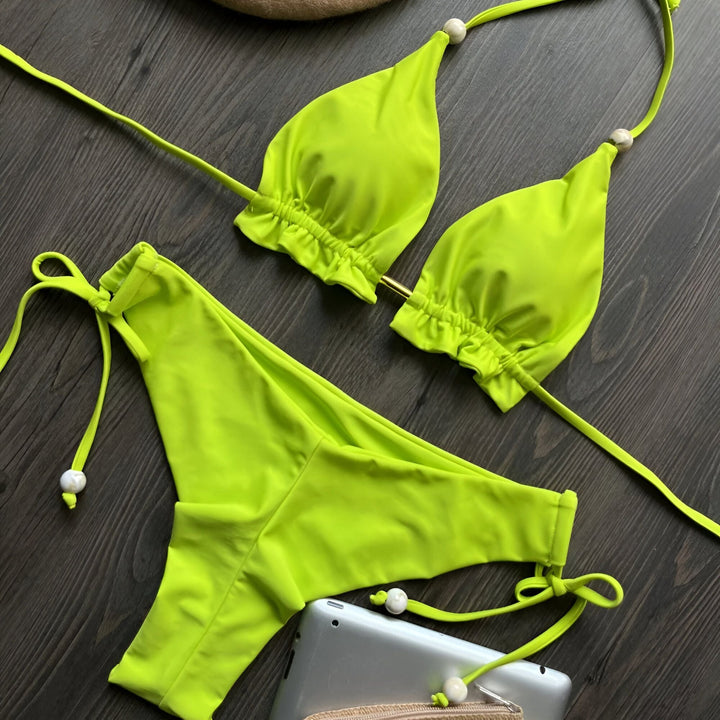 Image d'un ensemble de bikini vert citron vif sur une surface en bois foncé, comprenant un haut triangle et une culotte à nouer.