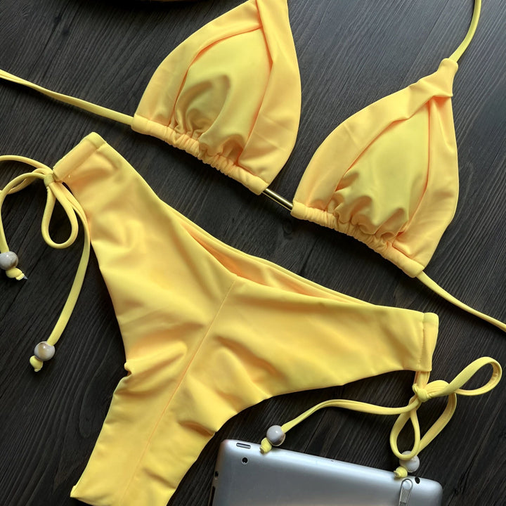 Image d'un ensemble de bikini vert olive avec un béret beige orné de perles sur un fond en bois foncé. Le maillot de bain est à la mode et l'accessoire ajoute une touche élégante.