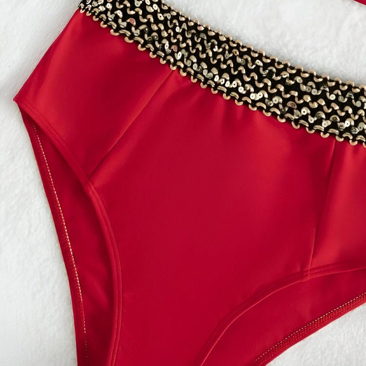 Vue arrière d'une femme portant un maillot de bain rouge deux pièces avec une ceinture dorée à la taille, mettant en valeur sa silhouette et ses courbes sous une lumière naturelle.