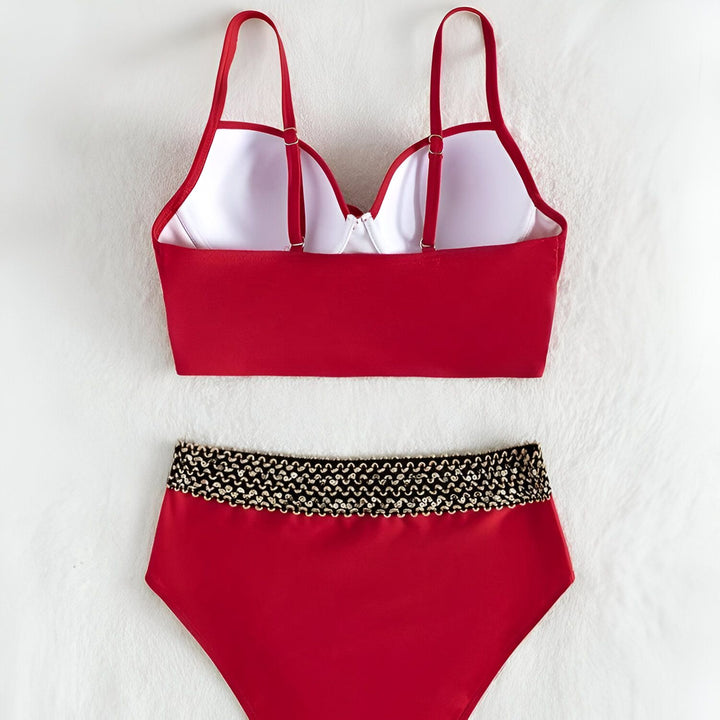 Gros plan d'un mannequin portant un maillot de bain rouge deux pièces taille haute avec une ceinture dorée décorative à la taille. Le haut est croisé sur le devant.