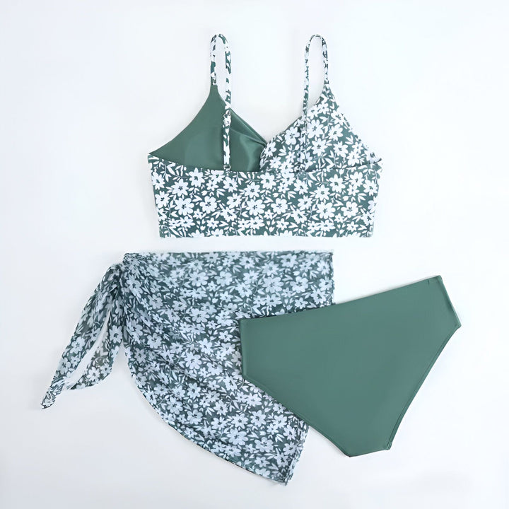 Ensemble de maillot de bain 3 pièces vert foncé avec motif floral blanc, comprenant un haut de bikini, un bas de maillot de bain uni et un paréo transparent assorti. Mode été, vêtements de plage.