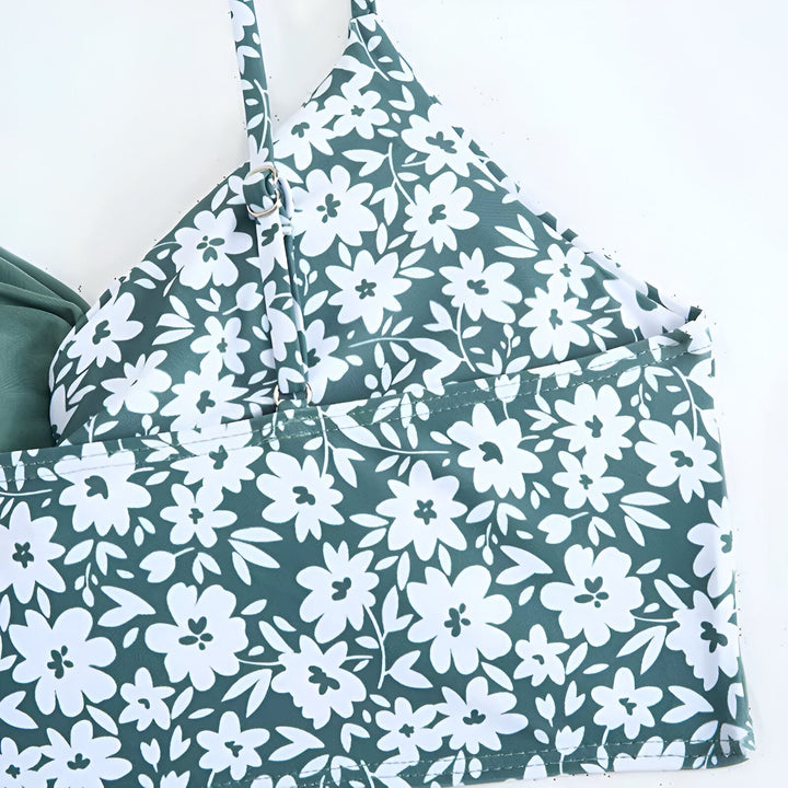 Ensemble de maillot de bain vert sauge avec un haut à fleurs, un bas uni et un paréo assorti. Chapeau de paille et lunettes de soleil blanches complètent la tenue estivale.