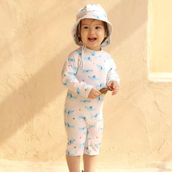 Combinaison de bain bébé à manches longues, blanche avec motif de petits chiens bleus et pois colorés, idéale pour protéger la peau du soleil.