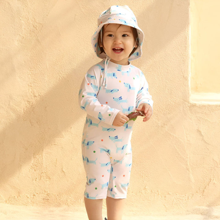 Combinaison de bain bébé à manches longues, blanche avec motif de petits chiens bleus et pois colorés, idéale pour protéger la peau du soleil.