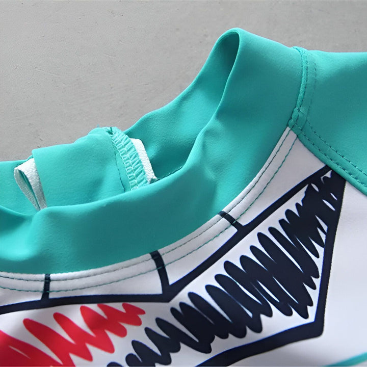 Gros plan sur un tissu imprimé blanc avec des motifs colorés (bleu, jaune, noir). Bordure turquoise visible. Détails de la couture apparente.