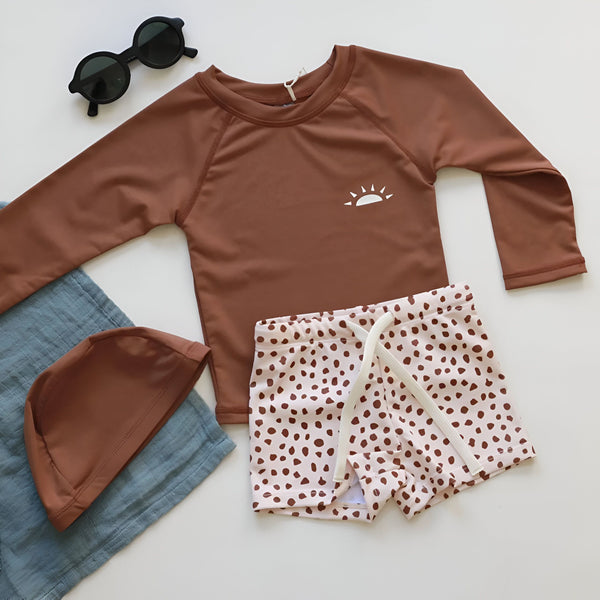 Gros plan sur un t-shirt de bain marron avec un logo de soleil blanc. Vêtement de protection solaire pour enfants, idéal pour la plage et la piscine. Tissu confortable et résistant.