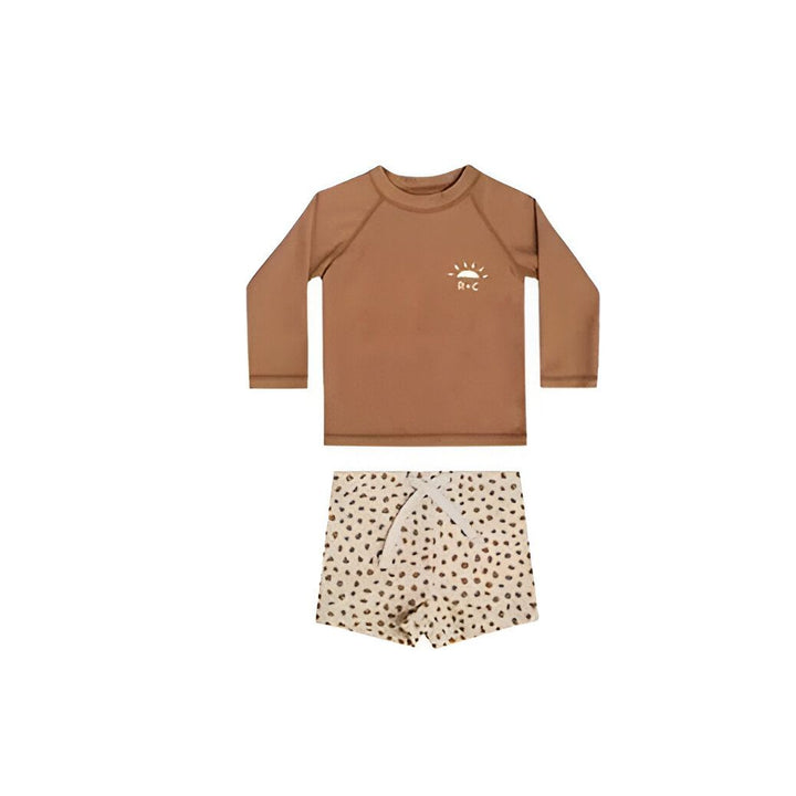 Vêtements de bain pour enfants. Haut de bain marron à manches longues avec motif de soleil blanc. Bas de bain rose clair à pois marron. Mode enfantine pour la plage.