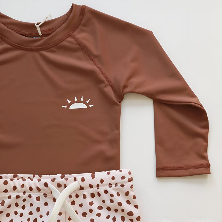 Ensemble de bain pour enfant. Haut de bain marron à manches longues avec logo soleil, et short de bain beige à pois. Idéal pour la plage et la piscine.