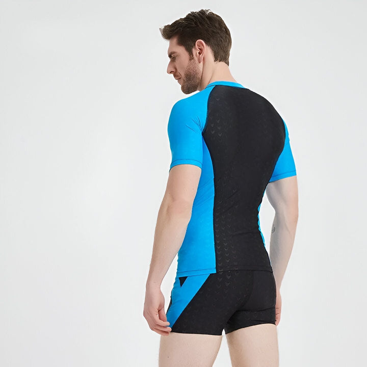 Homme en tenue de bain sportive noire et bleue, faisant des étirements. Idéal pour la natation et les sports nautiques. Vêtements de bain confortables et performants.