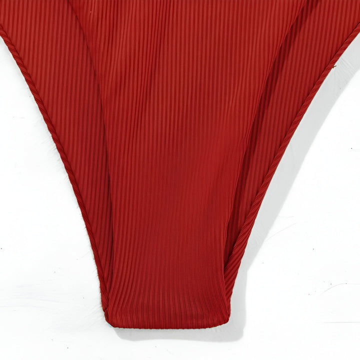 Femme en bikini rouge deux pièces, allongée sur un coussin. Manucure blanche, bague et bracelet. Panier en osier flou en arrière-plan.