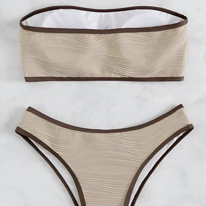 Ensemble de bikini beige texturé avec bordure marron, comprenant un haut bandeau et une culotte taille haute, sur un fond marbré blanc.