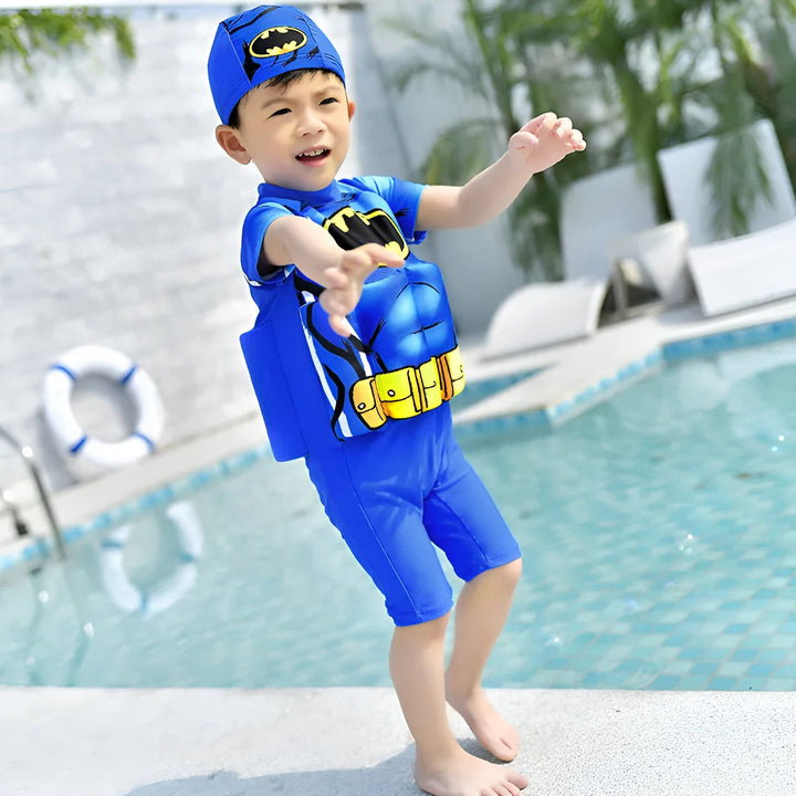 Combinaison de bain rose pour enfant avec flotteurs intégrés, accompagnée d'un chapeau assorti orné d'un chat marin, d'un tournesol et d'étoiles de mer, sur un fond de galets blancs. Idéal pour la piscine et les vacances.