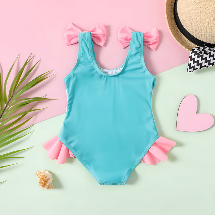 Maillot de bain turquoise pour enfants avec nœuds roses, chapeau de paille, feuille de palmier, coquillage et cœur sur fond rose et vert pastel. Mode d'été pour enfants.