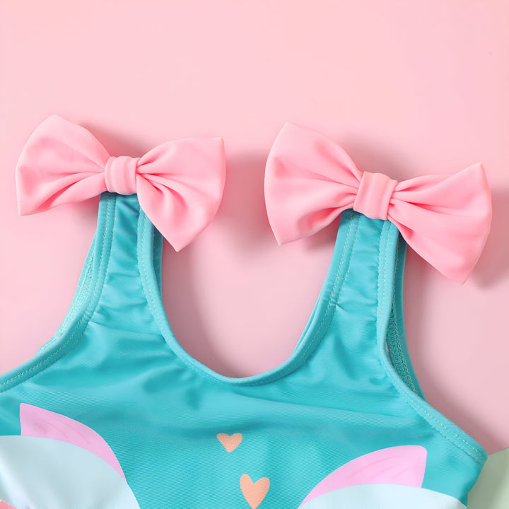 Maillot de bain enfant turquoise avec motif de deux cygnes roses s'embrassant et rubans roses sur les bretelles et volants roses sur les côtés. Idéal pour la plage ou la piscine.