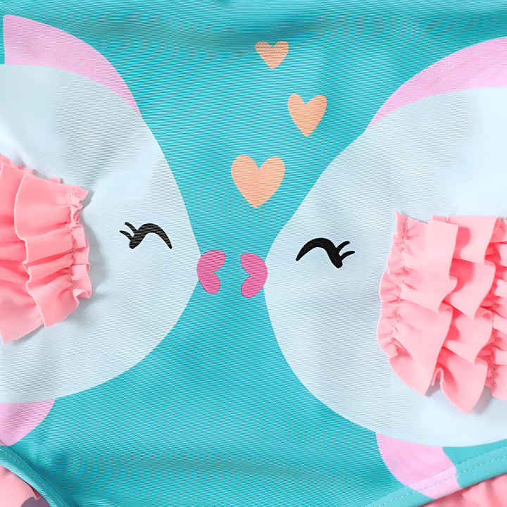 Maillot de bain turquoise pour enfant avec motif de deux poissons s'embrassant, orné de volants roses et de nœuds, avec décor de plage : chapeau de paille, coquillage, cœur rose et feuille de palmier.