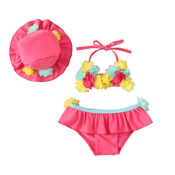 Ensemble de maillot de bain deux pièces pour bébé fille avec chapeau assorti, lunettes de soleil et une fleur tropicale blanche, sur un fond en bois. L'ensemble est bleu et rose, décoré de fleurs colorées.