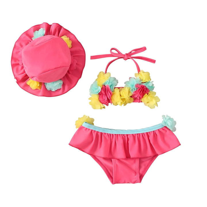 Ensemble de maillot de bain deux pièces pour bébé fille avec chapeau assorti, lunettes de soleil et une fleur tropicale blanche, sur un fond en bois. L'ensemble est bleu et rose, décoré de fleurs colorées.