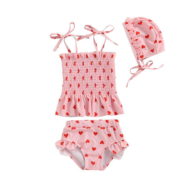 Gros plan d'un maillot de bain rose pâle à motifs de coeurs rouges. Haut smocké avec volant, et bas de bikini assorti. Idéal pour l'été ou la Saint-Valentin. Mode enfantine, tenue de plage.