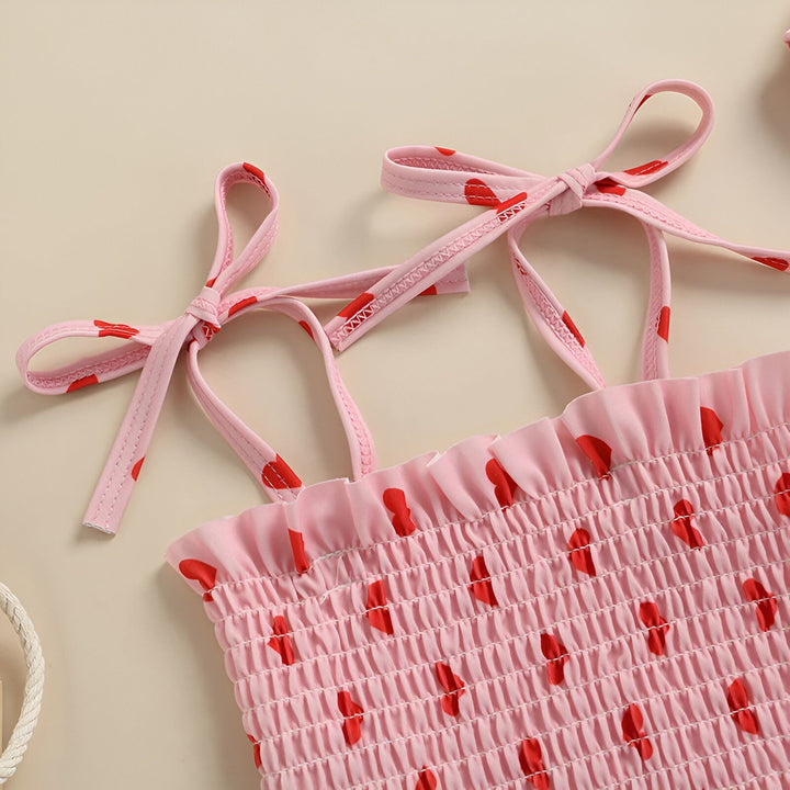 Maillot de bain une pièce rose à volants et motif de coeurs rouges pour bébé fille, accompagné d'un bonnet assorti. Style estival et adorable pour les petites nageuses.